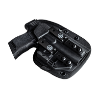 A black polymer holster containing a black handgun, shown from an angled top-down view against a transparent background. The holster features a quick-release clip with a circular crosshair logo and a textured grip on the pistol.