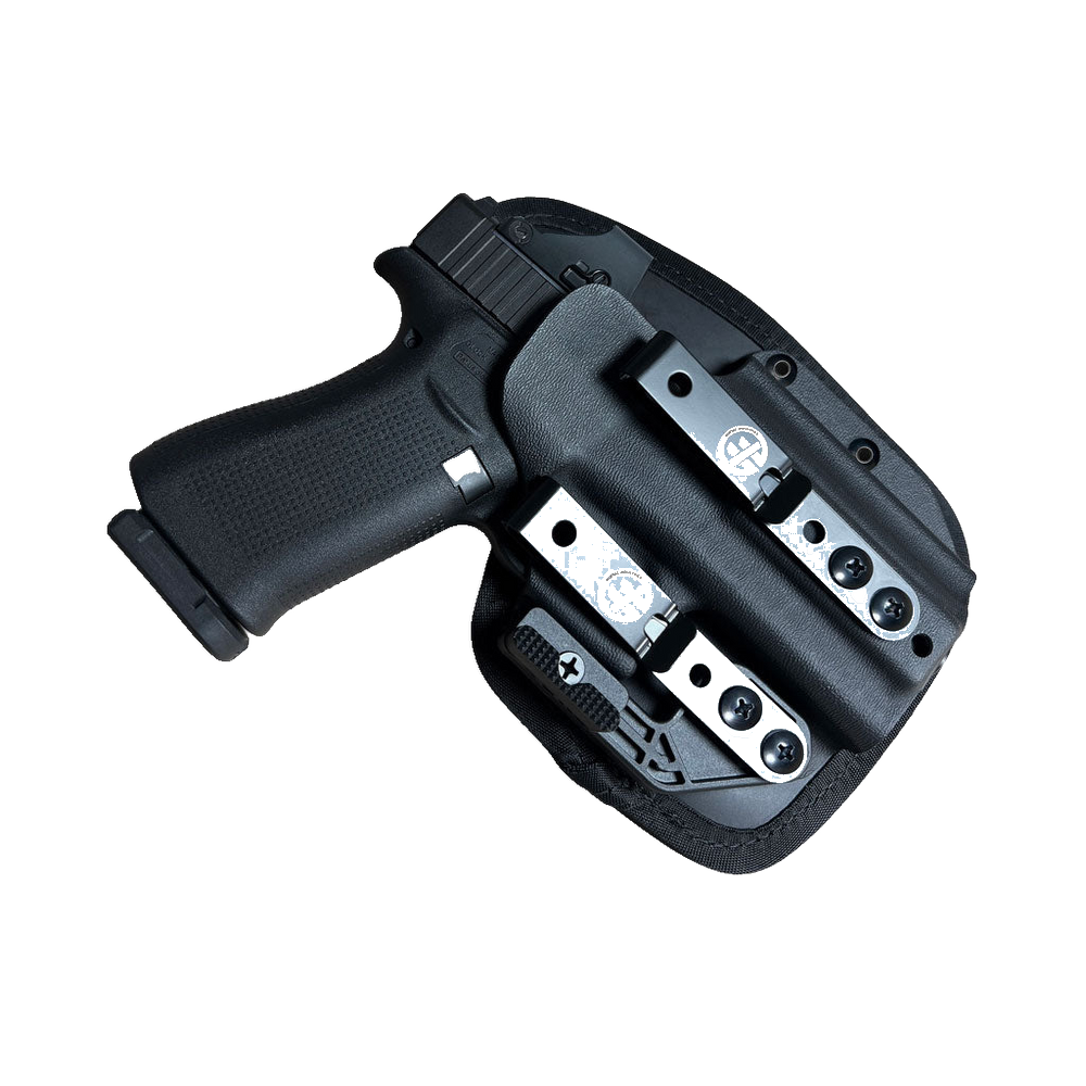 A black semi-automatic handgun in a black Kydex holster with silver metal quick-release buckles, shown against a transparent background.