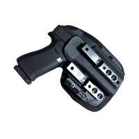 A black semi-automatic handgun in a black Kydex holster with silver metal quick-release buckles, shown against a transparent background.
